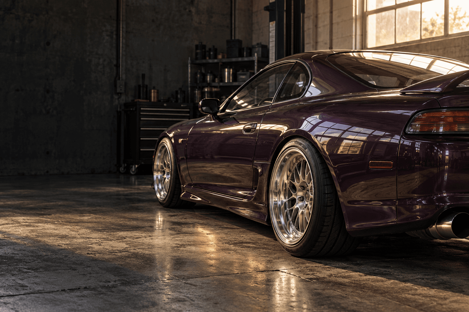 Plum sports coupe with polished aftermarket wheels in a sunlit workshop